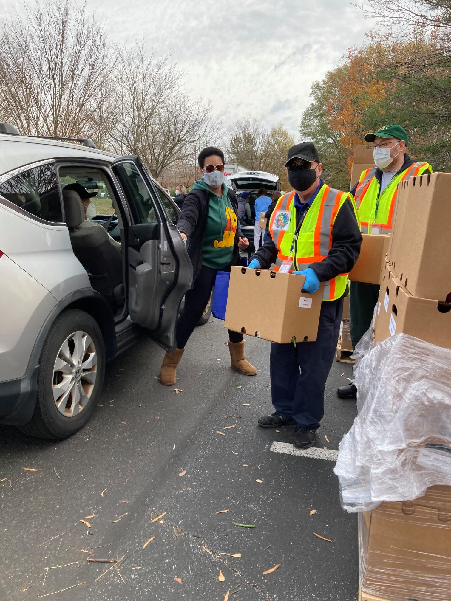 AAACERT members in safety vests hold boxes full of food; a car has pulled up and the door is open to receive food.